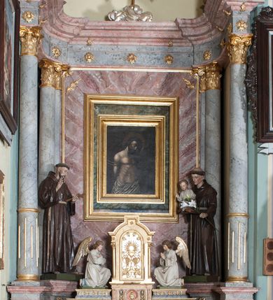 Zdjęcie nr 2: Nastawa ołtarzowa, odpowiadająca formie wnęki, jednoosiowa, jednokondygnacyjna ze zwieńczeniem, na podwójnym cokole. Mensa sarkofagowa, ustawiona na dwóch stopniach, wklęsło-wypukła, zwężająca się ku dołowi. Drewniana z marmurowym portatylem z napisem na odwrocie „Anno Domini MDCCCXCIX Die 1. Augusti Celsissimus ac Reverendissimus Dominus  JOANNES KNIAŹ DE KOZIELSKO PUZYNA Princeps Episcopus Cracoviensis altare hoc portatile consecravit Reliquiasque SS. Corduba et Rogatae Mill inclusit Rog Th Runowski Vice Kustos”. Na mensie ustawiono tabernakulum w formie sześcianu, na cokole, od frontu ujęte kolumnami we wnękach, całość zamknięta gzymsem w formie łuku nadwieszonego. Drzwiczki w profilowanej ramie, dekorowane płaskorzeźbionym przedstawieniem kielicha z hostią w glorii, w otoczeniu kiści winogron i z motywem maswerkowania. Cokół dekorowany trzema płycinami; zewnętrzne w formie stojącego prostokąta, zamkniętego łukiem półkolistym z ornamentem roślinnym; środkowa w formie medalionu z sercem gorejącym. Tabernakulum flankowane przez dwie figury klęczących aniołów, ustawionych na podwójnym cokole, dekorowanym ornamentem roślinnym. Kondygnacja nastawy ujęta dwiema parami kompozytowych kolumn, ustawionych w jednej linii; wewnętrzna para pod kątem. Podpory dźwigają pełne belkowanie, delikatnie wyłamane na ich osiach. W polu środkowym obraz z przedstawieniem Chrystusa u słupa, w profilowanej ramie w formie stojącego prostokąta. Na zasuwie przedstawienie Matki Boskiej Różańcowej ze św. Dominikiem. Pole flankowane przez figury św. Antoniego Padewskiego i św. Franciszka ustawione na niewielkich konsolkach. Na gzymsie płaskorzeźbione Oko Opatrzności w glorii promienistej, z obłokiem. Zwieńczenie w formie czterech kabłąków podtrzymujących diadem zdobiony lambrekinem, ze spływającą po bokach draperią; powyżej cztery kabłąki podtrzymujące krzyż i gorejące serce pośrodku. Cokoły zdobione płycinami z motywem rozet; w jednej trzeciej wysokości trzonów kolumn pierścienie. Fryz zdobiony rozetami. Struktura marmoryzowana w odcieniach jasnego różu i szarości; ornamentyka i detale złocone i srebrzone.