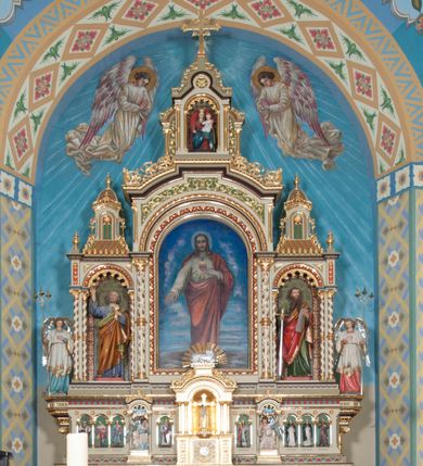 Zdjęcie nr 1: Nastawa ołtarzowa jednokondygnacyjna ze zwieńczeniem, trójosiowa, na cokole. Mensa prostopadłościenna, murowana, w drewnianej obudowie, z kamiennym blatem. Antepedium podzielone na trzy pola, wydzielone czterema kolumienkami. Zewnętrzne płyciny w formie leżącego prostokąta, z płaskorzeźbionymi przedstawieniami po lewej stronie ofiara Melchizedeka, po prawej ofiara Abrahama. W polu środkowym płycina w formie kwadratu, z stylizowanym maswerkowaniem i równoramiennym krzyżem pośrodku oraz rozetami w narożach. Na mensie tabernakulum na wysokiej, prostopadłościennej podstawie, w której znajdują się drzwiczki dekorowane hostią w glorii, flankowane pilastrami z dekoracją  ornamentem arabeskowym. Na osi tron wystawienia w formie niszy ujęty parą smukłych kolumienek podtrzymujących szerokie belkowanie przechodzące nad niszą w łuk. Gzyms wieńczy ornament roślinny, na środku na cokole postać baranka w glorii na księdze z siedmioma pieczęciami. Predella podzielona na trzy pola z występującymi do przodu dwiema niszami z figurami klęczących aniołów. W polach zewnętrznych trzy arkadki z płaskorzeźbionymi przedstawieniami świętych. W polu środkowym tabernakulum flankowane przed dwie arkadki z przedstawieniami świętych. Pierwsza kondygnacja utworzona z trzech arkad wydzielonych kolumnami, oś środkowa wyższa od bocznych. W polu środkowym obraz z przedstawieniem Najświętszego Serca Jezusa, w profilowanej ramie; archiwolta ujęta kolumienkami. Całość zamknięta silnie wysuniętym gzymsem o fantazyjnej linii. W osiach bocznych aedicule z posągami św. Piotra i św. Pawła, zwieńczone daszkiem z latarniami. Kondygnacja flankowana wielobocznymi wspornikami z figurami aniołów. Zwieńczenie w formie aediculi ujętej kolumienkami we wnękach oraz otwartymi półarkadami. Całość zamknięta gzymsem o fantazyjnej linii oraz krzyżem. W niszy figura Matki Boskiej z Dzieciątkiem. Cokoły zdobione płycinami z malowaną i złoconą dekoracja roślinną. Rama obrazu w polu środkowym dekorowana ornamentem roślinno-geometrycznym; archiwolta ornamentem roślinnym w formie liści. Powyżej płycina w kształcie łuku odcinkowego z rzeźbionym ornamentem roślinnym. Archiwolty arkad na osiach bocznych dekorowane ornamentem geometrycznym i stylizowanymi żabkami, w przyłuczach rozety; latarnie zdobione ornamentem roślinnym i stylizowanymi żabkami. Struktura polichromowana w kolorze kości słoniowej i szarym; płyciny i profilowania w kolorze czerwonym oraz zielonym, elementy dekoracyjne złocone.