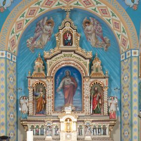 Zdjęcie nr 1: Nastawa ołtarzowa jednokondygnacyjna ze zwieńczeniem, trójosiowa, na cokole. Mensa prostopadłościenna, murowana, w drewnianej obudowie, z kamiennym blatem. Antepedium podzielone na trzy pola, wydzielone czterema kolumienkami. Zewnętrzne płyciny w formie leżącego prostokąta, z płaskorzeźbionymi przedstawieniami po lewej stronie ofiara Melchizedeka, po prawej ofiara Abrahama. W polu środkowym płycina w formie kwadratu, z stylizowanym maswerkowaniem i równoramiennym krzyżem pośrodku oraz rozetami w narożach. Na mensie tabernakulum na wysokiej, prostopadłościennej podstawie, w której znajdują się drzwiczki dekorowane hostią w glorii, flankowane pilastrami z dekoracją  ornamentem arabeskowym. Na osi tron wystawienia w formie niszy ujęty parą smukłych kolumienek podtrzymujących szerokie belkowanie przechodzące nad niszą w łuk. Gzyms wieńczy ornament roślinny, na środku na cokole postać baranka w glorii na księdze z siedmioma pieczęciami. Predella podzielona na trzy pola z występującymi do przodu dwiema niszami z figurami klęczących aniołów. W polach zewnętrznych trzy arkadki z płaskorzeźbionymi przedstawieniami świętych. W polu środkowym tabernakulum flankowane przed dwie arkadki z przedstawieniami świętych. Pierwsza kondygnacja utworzona z trzech arkad wydzielonych kolumnami, oś środkowa wyższa od bocznych. W polu środkowym obraz z przedstawieniem Najświętszego Serca Jezusa, w profilowanej ramie; archiwolta ujęta kolumienkami. Całość zamknięta silnie wysuniętym gzymsem o fantazyjnej linii. W osiach bocznych aedicule z posągami św. Piotra i św. Pawła, zwieńczone daszkiem z latarniami. Kondygnacja flankowana wielobocznymi wspornikami z figurami aniołów. Zwieńczenie w formie aediculi ujętej kolumienkami we wnękach oraz otwartymi półarkadami. Całość zamknięta gzymsem o fantazyjnej linii oraz krzyżem. W niszy figura Matki Boskiej z Dzieciątkiem. Cokoły zdobione płycinami z malowaną i złoconą dekoracja roślinną. Rama obrazu w polu środkowym dekorowana ornamentem roślinno-geometrycznym; archiwolta ornamentem roślinnym w formie liści. Powyżej płycina w kształcie łuku odcinkowego z rzeźbionym ornamentem roślinnym. Archiwolty arkad na osiach bocznych dekorowane ornamentem geometrycznym i stylizowanymi żabkami, w przyłuczach rozety; latarnie zdobione ornamentem roślinnym i stylizowanymi żabkami. Struktura polichromowana w kolorze kości słoniowej i szarym; płyciny i profilowania w kolorze czerwonym oraz zielonym, elementy dekoracyjne złocone.