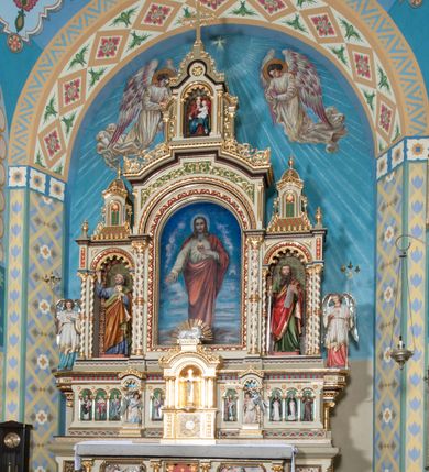 Zdjęcie nr 2: Nastawa ołtarzowa jednokondygnacyjna ze zwieńczeniem, trójosiowa, na cokole. Mensa prostopadłościenna, murowana, w drewnianej obudowie, z kamiennym blatem. Antepedium podzielone na trzy pola, wydzielone czterema kolumienkami. Zewnętrzne płyciny w formie leżącego prostokąta, z płaskorzeźbionymi przedstawieniami po lewej stronie ofiara Melchizedeka, po prawej ofiara Abrahama. W polu środkowym płycina w formie kwadratu, z stylizowanym maswerkowaniem i równoramiennym krzyżem pośrodku oraz rozetami w narożach. Na mensie tabernakulum na wysokiej, prostopadłościennej podstawie, w której znajdują się drzwiczki dekorowane hostią w glorii, flankowane pilastrami z dekoracją  ornamentem arabeskowym. Na osi tron wystawienia w formie niszy ujęty parą smukłych kolumienek podtrzymujących szerokie belkowanie przechodzące nad niszą w łuk. Gzyms wieńczy ornament roślinny, na środku na cokole postać baranka w glorii na księdze z siedmioma pieczęciami. Predella podzielona na trzy pola z występującymi do przodu dwiema niszami z figurami klęczących aniołów. W polach zewnętrznych trzy arkadki z płaskorzeźbionymi przedstawieniami świętych. W polu środkowym tabernakulum flankowane przed dwie arkadki z przedstawieniami świętych. Pierwsza kondygnacja utworzona z trzech arkad wydzielonych kolumnami, oś środkowa wyższa od bocznych. W polu środkowym obraz z przedstawieniem Najświętszego Serca Jezusa, w profilowanej ramie; archiwolta ujęta kolumienkami. Całość zamknięta silnie wysuniętym gzymsem o fantazyjnej linii. W osiach bocznych aedicule z posągami św. Piotra i św. Pawła, zwieńczone daszkiem z latarniami. Kondygnacja flankowana wielobocznymi wspornikami z figurami aniołów. Zwieńczenie w formie aediculi ujętej kolumienkami we wnękach oraz otwartymi półarkadami. Całość zamknięta gzymsem o fantazyjnej linii oraz krzyżem. W niszy figura Matki Boskiej z Dzieciątkiem. Cokoły zdobione płycinami z malowaną i złoconą dekoracja roślinną. Rama obrazu w polu środkowym dekorowana ornamentem roślinno-geometrycznym; archiwolta ornamentem roślinnym w formie liści. Powyżej płycina w kształcie łuku odcinkowego z rzeźbionym ornamentem roślinnym. Archiwolty arkad na osiach bocznych dekorowane ornamentem geometrycznym i stylizowanymi żabkami, w przyłuczach rozety; latarnie zdobione ornamentem roślinnym i stylizowanymi żabkami. Struktura polichromowana w kolorze kości słoniowej i szarym; płyciny i profilowania w kolorze czerwonym oraz zielonym, elementy dekoracyjne złocone.