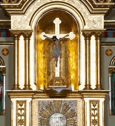 Zdjęcie nr 34: Nastawa ołtarzowa jednokondygnacyjna ze zwieńczeniem, trójosiowa, na cokole. Mensa prostopadłościenna, murowana, w drewnianej obudowie, z kamiennym blatem. Antepedium podzielone na trzy pola, wydzielone czterema kolumienkami. Zewnętrzne płyciny w formie leżącego prostokąta, z płaskorzeźbionymi przedstawieniami po lewej stronie ofiara Melchizedeka, po prawej ofiara Abrahama. W polu środkowym płycina w formie kwadratu, z stylizowanym maswerkowaniem i równoramiennym krzyżem pośrodku oraz rozetami w narożach. Na mensie tabernakulum na wysokiej, prostopadłościennej podstawie, w której znajdują się drzwiczki dekorowane hostią w glorii, flankowane pilastrami z dekoracją  ornamentem arabeskowym. Na osi tron wystawienia w formie niszy ujęty parą smukłych kolumienek podtrzymujących szerokie belkowanie przechodzące nad niszą w łuk. Gzyms wieńczy ornament roślinny, na środku na cokole postać baranka w glorii na księdze z siedmioma pieczęciami. Predella podzielona na trzy pola z występującymi do przodu dwiema niszami z figurami klęczących aniołów. W polach zewnętrznych trzy arkadki z płaskorzeźbionymi przedstawieniami świętych. W polu środkowym tabernakulum flankowane przed dwie arkadki z przedstawieniami świętych. Pierwsza kondygnacja utworzona z trzech arkad wydzielonych kolumnami, oś środkowa wyższa od bocznych. W polu środkowym obraz z przedstawieniem Najświętszego Serca Jezusa, w profilowanej ramie; archiwolta ujęta kolumienkami. Całość zamknięta silnie wysuniętym gzymsem o fantazyjnej linii. W osiach bocznych aedicule z posągami św. Piotra i św. Pawła, zwieńczone daszkiem z latarniami. Kondygnacja flankowana wielobocznymi wspornikami z figurami aniołów. Zwieńczenie w formie aediculi ujętej kolumienkami we wnękach oraz otwartymi półarkadami. Całość zamknięta gzymsem o fantazyjnej linii oraz krzyżem. W niszy figura Matki Boskiej z Dzieciątkiem. Cokoły zdobione płycinami z malowaną i złoconą dekoracja roślinną. Rama obrazu w polu środkowym dekorowana ornamentem roślinno-geometrycznym; archiwolta ornamentem roślinnym w formie liści. Powyżej płycina w kształcie łuku odcinkowego z rzeźbionym ornamentem roślinnym. Archiwolty arkad na osiach bocznych dekorowane ornamentem geometrycznym i stylizowanymi żabkami, w przyłuczach rozety; latarnie zdobione ornamentem roślinnym i stylizowanymi żabkami. Struktura polichromowana w kolorze kości słoniowej i szarym; płyciny i profilowania w kolorze czerwonym oraz zielonym, elementy dekoracyjne złocone.