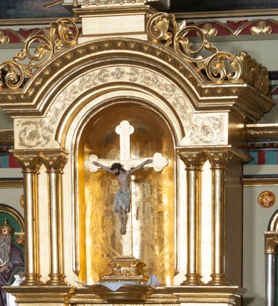 Zdjęcie nr 33: Nastawa ołtarzowa jednokondygnacyjna ze zwieńczeniem, trójosiowa, na cokole. Mensa prostopadłościenna, murowana, w drewnianej obudowie, z kamiennym blatem. Antepedium podzielone na trzy pola, wydzielone czterema kolumienkami. Zewnętrzne płyciny w formie leżącego prostokąta, z płaskorzeźbionymi przedstawieniami po lewej stronie ofiara Melchizedeka, po prawej ofiara Abrahama. W polu środkowym płycina w formie kwadratu, z stylizowanym maswerkowaniem i równoramiennym krzyżem pośrodku oraz rozetami w narożach. Na mensie tabernakulum na wysokiej, prostopadłościennej podstawie, w której znajdują się drzwiczki dekorowane hostią w glorii, flankowane pilastrami z dekoracją  ornamentem arabeskowym. Na osi tron wystawienia w formie niszy ujęty parą smukłych kolumienek podtrzymujących szerokie belkowanie przechodzące nad niszą w łuk. Gzyms wieńczy ornament roślinny, na środku na cokole postać baranka w glorii na księdze z siedmioma pieczęciami. Predella podzielona na trzy pola z występującymi do przodu dwiema niszami z figurami klęczących aniołów. W polach zewnętrznych trzy arkadki z płaskorzeźbionymi przedstawieniami świętych. W polu środkowym tabernakulum flankowane przed dwie arkadki z przedstawieniami świętych. Pierwsza kondygnacja utworzona z trzech arkad wydzielonych kolumnami, oś środkowa wyższa od bocznych. W polu środkowym obraz z przedstawieniem Najświętszego Serca Jezusa, w profilowanej ramie; archiwolta ujęta kolumienkami. Całość zamknięta silnie wysuniętym gzymsem o fantazyjnej linii. W osiach bocznych aedicule z posągami św. Piotra i św. Pawła, zwieńczone daszkiem z latarniami. Kondygnacja flankowana wielobocznymi wspornikami z figurami aniołów. Zwieńczenie w formie aediculi ujętej kolumienkami we wnękach oraz otwartymi półarkadami. Całość zamknięta gzymsem o fantazyjnej linii oraz krzyżem. W niszy figura Matki Boskiej z Dzieciątkiem. Cokoły zdobione płycinami z malowaną i złoconą dekoracja roślinną. Rama obrazu w polu środkowym dekorowana ornamentem roślinno-geometrycznym; archiwolta ornamentem roślinnym w formie liści. Powyżej płycina w kształcie łuku odcinkowego z rzeźbionym ornamentem roślinnym. Archiwolty arkad na osiach bocznych dekorowane ornamentem geometrycznym i stylizowanymi żabkami, w przyłuczach rozety; latarnie zdobione ornamentem roślinnym i stylizowanymi żabkami. Struktura polichromowana w kolorze kości słoniowej i szarym; płyciny i profilowania w kolorze czerwonym oraz zielonym, elementy dekoracyjne złocone.