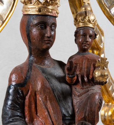 Zdjęcie nr 3: Feretron z figurą Matki Boskiej z Dzieciątkiem umieszczoną pod ozdobnym baldachimem, na prostopadłościennej podstawie. Maria została ukazana całopostaciowo, w lekkim kontrapoście. Prawą rękę trzyma wyciągniętą przed sobą na wysokości pasa; lewą podtrzymuje Dzieciątko. Karnacja Marii i Dzieciątka ciemnobrązowa. Twarz Matki Boskiej owalna, o pełnych policzkach i drobnych regularnych rysach. Maria jest ubrana w ciemnobrązową suknię oraz drapowany, rudy płaszcz z ciemną lamówką. Welon na głowie zaznaczony za pomocą malowanego konturu. Dzieciątko siedzi, stopy ma wyciągnięte przed siebie, prawą rękę unosi w geście błogosławieństwa, w lewej trzyma jabłko królewskie. Twarz małego Jezusa jest owalna, czoło wysokie, okolone ciemnymi puklami. Na głowach Marii i Dzieciątka złote korony zamknięte. Rzeźba wtórnie umieszczona w feretronie – na postumencie, ujęta w cztery ślimacznice łączące się pod okrągłym lambrekinem zwieńczonym promienistą glorią z centralnie umieszczonym monogramem Marii.