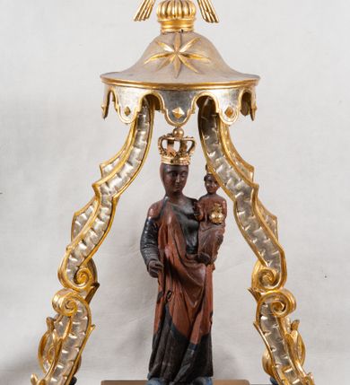 Zdjęcie nr 1: Feretron z figurą Matki Boskiej z Dzieciątkiem umieszczoną pod ozdobnym baldachimem, na prostopadłościennej podstawie. Maria została ukazana całopostaciowo, w lekkim kontrapoście. Prawą rękę trzyma wyciągniętą przed sobą na wysokości pasa; lewą podtrzymuje Dzieciątko. Karnacja Marii i Dzieciątka ciemnobrązowa. Twarz Matki Boskiej owalna, o pełnych policzkach i drobnych regularnych rysach. Maria jest ubrana w ciemnobrązową suknię oraz drapowany, rudy płaszcz z ciemną lamówką. Welon na głowie zaznaczony za pomocą malowanego konturu. Dzieciątko siedzi, stopy ma wyciągnięte przed siebie, prawą rękę unosi w geście błogosławieństwa, w lewej trzyma jabłko królewskie. Twarz małego Jezusa jest owalna, czoło wysokie, okolone ciemnymi puklami. Na głowach Marii i Dzieciątka złote korony zamknięte. Rzeźba wtórnie umieszczona w feretronie – na postumencie, ujęta w cztery ślimacznice łączące się pod okrągłym lambrekinem zwieńczonym promienistą glorią z centralnie umieszczonym monogramem Marii.