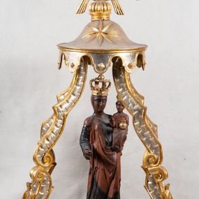 Zdjęcie nr 1: Feretron z figurą Matki Boskiej z Dzieciątkiem umieszczoną pod ozdobnym baldachimem, na prostopadłościennej podstawie. Maria została ukazana całopostaciowo, w lekkim kontrapoście. Prawą rękę trzyma wyciągniętą przed sobą na wysokości pasa; lewą podtrzymuje Dzieciątko. Karnacja Marii i Dzieciątka ciemnobrązowa. Twarz Matki Boskiej owalna, o pełnych policzkach i drobnych regularnych rysach. Maria jest ubrana w ciemnobrązową suknię oraz drapowany, rudy płaszcz z ciemną lamówką. Welon na głowie zaznaczony za pomocą malowanego konturu. Dzieciątko siedzi, stopy ma wyciągnięte przed siebie, prawą rękę unosi w geście błogosławieństwa, w lewej trzyma jabłko królewskie. Twarz małego Jezusa jest owalna, czoło wysokie, okolone ciemnymi puklami. Na głowach Marii i Dzieciątka złote korony zamknięte. Rzeźba wtórnie umieszczona w feretronie – na postumencie, ujęta w cztery ślimacznice łączące się pod okrągłym lambrekinem zwieńczonym promienistą glorią z centralnie umieszczonym monogramem Marii.