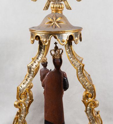 Zdjęcie nr 4: Feretron z figurą Matki Boskiej z Dzieciątkiem umieszczoną pod ozdobnym baldachimem, na prostopadłościennej podstawie. Maria została ukazana całopostaciowo, w lekkim kontrapoście. Prawą rękę trzyma wyciągniętą przed sobą na wysokości pasa; lewą podtrzymuje Dzieciątko. Karnacja Marii i Dzieciątka ciemnobrązowa. Twarz Matki Boskiej owalna, o pełnych policzkach i drobnych regularnych rysach. Maria jest ubrana w ciemnobrązową suknię oraz drapowany, rudy płaszcz z ciemną lamówką. Welon na głowie zaznaczony za pomocą malowanego konturu. Dzieciątko siedzi, stopy ma wyciągnięte przed siebie, prawą rękę unosi w geście błogosławieństwa, w lewej trzyma jabłko królewskie. Twarz małego Jezusa jest owalna, czoło wysokie, okolone ciemnymi puklami. Na głowach Marii i Dzieciątka złote korony zamknięte. Rzeźba wtórnie umieszczona w feretronie – na postumencie, ujęta w cztery ślimacznice łączące się pod okrągłym lambrekinem zwieńczonym promienistą glorią z centralnie umieszczonym monogramem Marii.