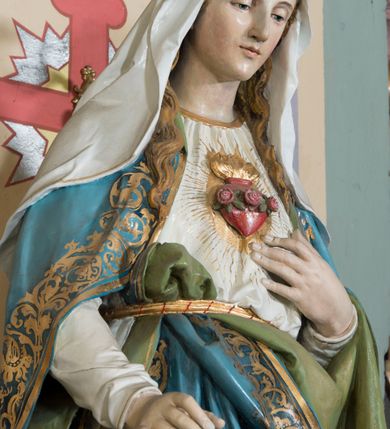 Zdjęcie nr 2: Rzeźba pełna, na cokole, przedstawiająca typ ikonograficzny  Najświętsze Serce Marii. Matka Boska została ukazana całopostaciowo, frontalnie, w lekkim kontrapoście. Głowę ma nieznacznie pochyloną do przodu, karnację jasną, rysy twarzy delikatne, powieki wpółprzymknięte. Jasne, falowane włosy dzielące się w pukle opadają na ramiona i dekolt. Maria jest ubrana w białą suknię przepasaną złotym sznurem. Na ramiona ma zarzucony błękitny, podbity zielenią płaszcz zdobiony przy brzegach złotą lamówką i złotym ornamentem roślinnym, a na głowę biały welon opadający na plecy i ramiona. Prawą rękę przyciska do piersi, na której widoczne gorejące złotym płomieniem, czerwone serce oplecione różanym wieńcem, lewą wyciąga przed siebie. 