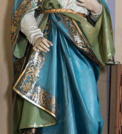 Zdjęcie nr 1: Rzeźba pełna, na cokole, przedstawiająca typ ikonograficzny  Najświętsze Serce Marii. Matka Boska została ukazana całopostaciowo, frontalnie, w lekkim kontrapoście. Głowę ma nieznacznie pochyloną do przodu, karnację jasną, rysy twarzy delikatne, powieki wpółprzymknięte. Jasne, falowane włosy dzielące się w pukle opadają na ramiona i dekolt. Maria jest ubrana w białą suknię przepasaną złotym sznurem. Na ramiona ma zarzucony błękitny, podbity zielenią płaszcz zdobiony przy brzegach złotą lamówką i złotym ornamentem roślinnym, a na głowę biały welon opadający na plecy i ramiona. Prawą rękę przyciska do piersi, na której widoczne gorejące złotym płomieniem, czerwone serce oplecione różanym wieńcem, lewą wyciąga przed siebie. 