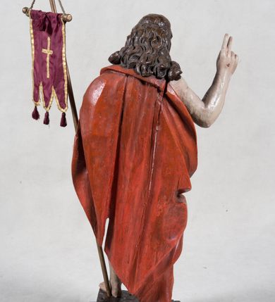 Zdjęcie nr 6: Rzeźba pełna ukazująca Chrystusa Zmartwychwstałego przedstawionego całopostaciowo, w lekkim kontrapoście, z delikatnie zaznaczoną muskulaturą i głową lekko opuszczoną. Jezus ma jasną karnację, twarz pociągłą o prostym nosie, okoloną długą brodą i falującymi brązowymi włosami spływającymi na plecy i prawe ramię. Jest ubrany w udrapowany czerwony płaszcz w diagonalnym układzie zarzucony na lewe ramię i owijający się wokół prawego biodra, łączący się pod lewą ręką. W lewej dłoni wtórnie dodana chorągiew w postaci purpurowej tkaniny z krzyżem na drewnianym drzewcu z resztkami złocenia, prawa dłoń wzniesiona w geście błogosławieństwa. Postać ustawiona na niewysokim postumencie imitującym skalny blok. 