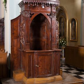 Zdjęcie nr 1: Drewniany konfesjonał ustawiony na jednostopniowym podwyższeniu na rzucie zbliżonym do prostokąta. Na profilowanym cokole drzwiczki wypukłe, wypełnione prostokątną płyciną, flankowane podobnymi, ale węższymi polami. Boki konfesjonału gładkie, przeprute otworami, z dostawionymi klęcznikami i zamknięte z obu stron wąskimi ściankami z płycinami, zakończonymi od góry skośnie. Baldachim z trójkątnym frontonem posadowiony na pilastrach korynckich dźwigających belkowanie dekorowane na środku leżącym rombem. Otwór zamknięty łukiem ostrym z trójliśćmi w przyłuczach, flankowany uszakami utworzonymi z liści i wolut odchodzących od centralnie ulokowanej rozety. Fronton wypukły, z umieszczonymi na środku skrzyżowanymi kluczami Piotrowymi, z rozetą na środku, od dołu dekorowany lambrekinem. Zaplecek dekorowany płycinami w kształcie leżących prostokątów. Struktura bejcowana na ciemnobrązowo. 