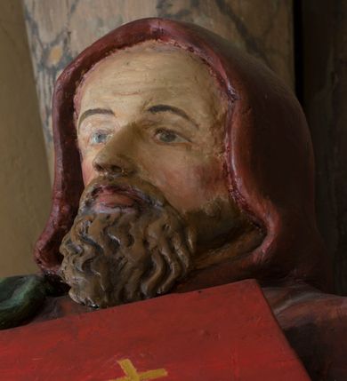 Zdjęcie nr 5: Rzeźba drążona, na cokole. Święty Cyryl został ukazany całopostaciowo, zwrócony nieznacznie w lewo z korpusem przechylonym na tę stronę, w kontrapoście. Ma owalną twarz o jasnej karnacji, wysokim czole, niebieskich oczach o kącikach zewnętrznych opadających w dół, niewielkim prostym nosie i małych ustach; falowana, jasnobrązowa broda opada mu na pierś. Jest ubrany w długi ciemnoczerwony habit przewiązany w pasie, z kapturem założonym na głowę. Habit opada do ziemi, łamiąc się w grube fałdy, spod niego wystają fragmenty butów. Na habit ma zarzucony na prawe ramię, udrapowany płaszcz w kolorze zieleni. W prawej dłoni Cyryl trzyma krzyż misyjny, lewą podtrzymuje rąbek płaszcza i księgę w czerwonej oprawie ze złotym krzyżem. Polichromia w partiach ciała naturalistyczna. 