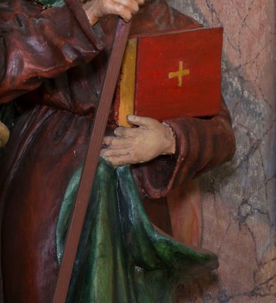 Zdjęcie nr 3: Rzeźba drążona, na cokole. Święty Cyryl został ukazany całopostaciowo, zwrócony nieznacznie w lewo z korpusem przechylonym na tę stronę, w kontrapoście. Ma owalną twarz o jasnej karnacji, wysokim czole, niebieskich oczach o kącikach zewnętrznych opadających w dół, niewielkim prostym nosie i małych ustach; falowana, jasnobrązowa broda opada mu na pierś. Jest ubrany w długi ciemnoczerwony habit przewiązany w pasie, z kapturem założonym na głowę. Habit opada do ziemi, łamiąc się w grube fałdy, spod niego wystają fragmenty butów. Na habit ma zarzucony na prawe ramię, udrapowany płaszcz w kolorze zieleni. W prawej dłoni Cyryl trzyma krzyż misyjny, lewą podtrzymuje rąbek płaszcza i księgę w czerwonej oprawie ze złotym krzyżem. Polichromia w partiach ciała naturalistyczna. 