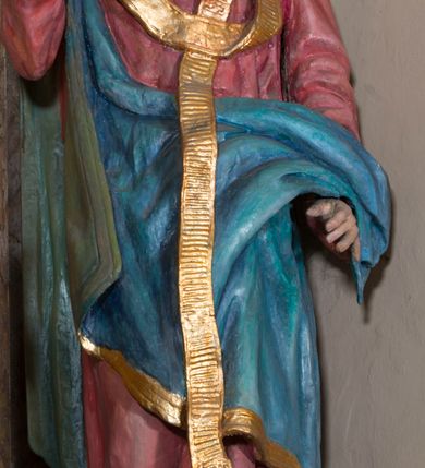 Zdjęcie nr 3: Rzeźba drążona, na cokole. Święty Metody został ukazany całopostaciowo, frontalnie, z głową zwróconą nieznacznie w lewo. Ma prostokątną twarz o jasnej karnacji, wysokim czole, brązowych oczach, prostym nosie i małych ustach. Falowana, ciemnobrązowa, rozdzielająca się w dwa pukle broda opada mu na pierś, a falowane włosy na ramiona i plecy. Jest ubrany w długi, ciemnoczerwony habit przewiązany w pasie, z kapturem wyłożonym na plecy. Habit opada do ziemi, łamiąc się w grube fałdy, na nim ma przewieszony złoty paliusz. Spod habitu wystają fragmenty odzianych w sandały stóp. Na habit ma zarzucony przez prawe ramię, udrapowany płaszcz w kolorze niebieskim. Metody unosi prawą dłoń w geście błogosławieństwa, lewą podtrzymuje fałdy płaszcza. Polichromia w partiach ciała naturalistyczna.