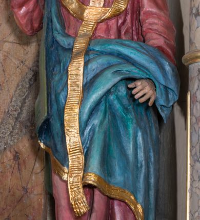 Zdjęcie nr 1: Rzeźba drążona, na cokole. Święty Metody został ukazany całopostaciowo, frontalnie, z głową zwróconą nieznacznie w lewo. Ma prostokątną twarz o jasnej karnacji, wysokim czole, brązowych oczach, prostym nosie i małych ustach. Falowana, ciemnobrązowa, rozdzielająca się w dwa pukle broda opada mu na pierś, a falowane włosy na ramiona i plecy. Jest ubrany w długi, ciemnoczerwony habit przewiązany w pasie, z kapturem wyłożonym na plecy. Habit opada do ziemi, łamiąc się w grube fałdy, na nim ma przewieszony złoty paliusz. Spod habitu wystają fragmenty odzianych w sandały stóp. Na habit ma zarzucony przez prawe ramię, udrapowany płaszcz w kolorze niebieskim. Metody unosi prawą dłoń w geście błogosławieństwa, lewą podtrzymuje fałdy płaszcza. Polichromia w partiach ciała naturalistyczna.