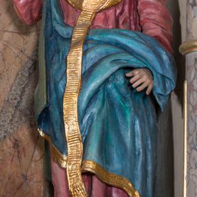 Zdjęcie nr 1: Rzeźba drążona, na cokole. Święty Metody został ukazany całopostaciowo, frontalnie, z głową zwróconą nieznacznie w lewo. Ma prostokątną twarz o jasnej karnacji, wysokim czole, brązowych oczach, prostym nosie i małych ustach. Falowana, ciemnobrązowa, rozdzielająca się w dwa pukle broda opada mu na pierś, a falowane włosy na ramiona i plecy. Jest ubrany w długi, ciemnoczerwony habit przewiązany w pasie, z kapturem wyłożonym na plecy. Habit opada do ziemi, łamiąc się w grube fałdy, na nim ma przewieszony złoty paliusz. Spod habitu wystają fragmenty odzianych w sandały stóp. Na habit ma zarzucony przez prawe ramię, udrapowany płaszcz w kolorze niebieskim. Metody unosi prawą dłoń w geście błogosławieństwa, lewą podtrzymuje fałdy płaszcza. Polichromia w partiach ciała naturalistyczna.