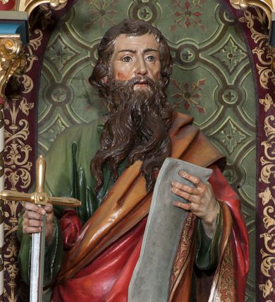 Zdjęcie nr 1: Rzeźba pełna (?) na cokole przedstawiająca św. Pawła ukazanego w całej postaci, frontalnie, z głową zwróconą nieznacznie w lewo. Święty prawą ręką chwyta za ostrze opartego o ziemię miecza, w lewej trzyma rozwiniętą kartę. Ma prostokątną twarz z brązowymi szeroko otwartymi oczami, prostym nosem oraz rozchylonymi ustami. Okalają ją ciemnobrązowe włosy, które spływając falami, zasłaniają uszy. Święty ma brodę sięgającą piersi, dzielącą się w pukle oraz wąsy. Jest ubrany w zieloną tunikę z szerokimi rękawami oraz podbity pomarańczowym materiałem czerwony płaszcz, dekorowany złotą lamówką i ornamentem roślinnym tej samej barwy przechodzący przez lewy bark i przytrzymany pod prawym łokciem. Tkaniny gną się grubymi, równoległymi fałdami. W partiach ciała polichromia naturalistyczna, atrybuty złocone i srebrzone.