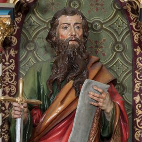 Zdjęcie nr 1: Rzeźba pełna (?) na cokole przedstawiająca św. Pawła ukazanego w całej postaci, frontalnie, z głową zwróconą nieznacznie w lewo. Święty prawą ręką chwyta za ostrze opartego o ziemię miecza, w lewej trzyma rozwiniętą kartę. Ma prostokątną twarz z brązowymi szeroko otwartymi oczami, prostym nosem oraz rozchylonymi ustami. Okalają ją ciemnobrązowe włosy, które spływając falami, zasłaniają uszy. Święty ma brodę sięgającą piersi, dzielącą się w pukle oraz wąsy. Jest ubrany w zieloną tunikę z szerokimi rękawami oraz podbity pomarańczowym materiałem czerwony płaszcz, dekorowany złotą lamówką i ornamentem roślinnym tej samej barwy przechodzący przez lewy bark i przytrzymany pod prawym łokciem. Tkaniny gną się grubymi, równoległymi fałdami. W partiach ciała polichromia naturalistyczna, atrybuty złocone i srebrzone.