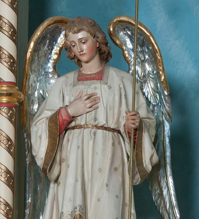 Zdjęcie nr 4: Ustawione na niewysokich cokołach pełnoplastyczne figury aniołów trzymających trójramienne świeczniki osadzone na długich trzonach. Oba spoglądają w dół, stoją w lekkim kontrapoście, a wolną rękę składają na piersi. Mają owalne twarze, małe oczy, wąskie nosy oraz usta. Jasnobrązowe, falowane włosy spływają im na karki. Ubrane są w długie suknie (anioł z lewej w niebieską, z prawej w czerwoną) i nałożone na nie białe tuniki z długimi rozszerzającymi się rękawami, wykończone złotą lamówką, przewiązane w pasie. Skrzydła mają złożone, srebrne o złoconych w górnej partii brzegach. Polichromia w partiach ciała naturalistyczna. 
