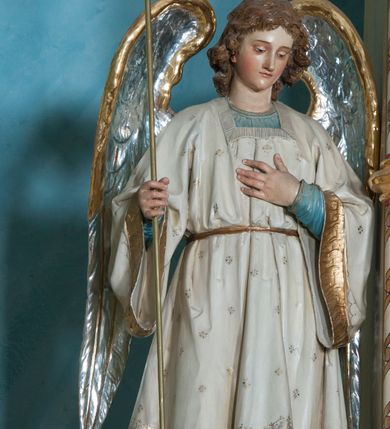 Zdjęcie nr 3: Ustawione na niewysokich cokołach pełnoplastyczne figury aniołów trzymających trójramienne świeczniki osadzone na długich trzonach. Oba spoglądają w dół, stoją w lekkim kontrapoście, a wolną rękę składają na piersi. Mają owalne twarze, małe oczy, wąskie nosy oraz usta. Jasnobrązowe, falowane włosy spływają im na karki. Ubrane są w długie suknie (anioł z lewej w niebieską, z prawej w czerwoną) i nałożone na nie białe tuniki z długimi rozszerzającymi się rękawami, wykończone złotą lamówką, przewiązane w pasie. Skrzydła mają złożone, srebrne o złoconych w górnej partii brzegach. Polichromia w partiach ciała naturalistyczna. 