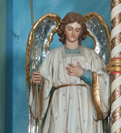 Zdjęcie nr 1: Ustawione na niewysokich cokołach pełnoplastyczne figury aniołów trzymających trójramienne świeczniki osadzone na długich trzonach. Oba spoglądają w dół, stoją w lekkim kontrapoście, a wolną rękę składają na piersi. Mają owalne twarze, małe oczy, wąskie nosy oraz usta. Jasnobrązowe, falowane włosy spływają im na karki. Ubrane są w długie suknie (anioł z lewej w niebieską, z prawej w czerwoną) i nałożone na nie białe tuniki z długimi rozszerzającymi się rękawami, wykończone złotą lamówką, przewiązane w pasie. Skrzydła mają złożone, srebrne o złoconych w górnej partii brzegach. Polichromia w partiach ciała naturalistyczna. 