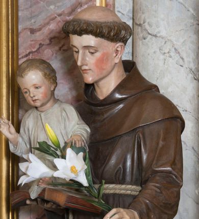 Zdjęcie nr 1: Rzeźba pełna przedstawiająca stojącego św. Antoniego Padewskiego z Dzieciątkiem Jezus. Święty ukazany w delikatnym kontrapoście, z głową lekko pochyloną. Oczy ma opuszczone, nos prosty, usta wąskie, na głowie tonsurę, włosy ciemne. Święty jest ubrany w brązowy habit franciszkański przepasany jasnym sznurem z węzłami. Na prawej ręce trzyma księgę, na której siedzi ubrane w białą sukienkę Dzieciątko, w lewej kwiat lilii. Polichromia w partiach ciała naturalistyczna.