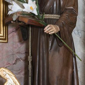 Zdjęcie nr 1: Rzeźba pełna przedstawiająca stojącego św. Antoniego Padewskiego z Dzieciątkiem Jezus. Święty ukazany w delikatnym kontrapoście, z głową lekko pochyloną. Oczy ma opuszczone, nos prosty, usta wąskie, na głowie tonsurę, włosy ciemne. Święty jest ubrany w brązowy habit franciszkański przepasany jasnym sznurem z węzłami. Na prawej ręce trzyma księgę, na której siedzi ubrane w białą sukienkę Dzieciątko, w lewej kwiat lilii. Polichromia w partiach ciała naturalistyczna.