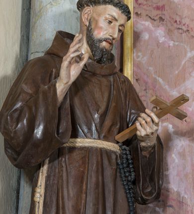 Zdjęcie nr 3: Rzeźba pełna przedstawiająca stojącego św. Franciszka. Święty ukazany frontalnie, z głową lekko pochyloną. Oczy ma opuszczone, nos prosty, usta wąskie; na głowie tonsurę, włosy ciemne, broda dzieli się w dwa pukle. Święty jest ubrany w brązowy habit franciszkański przepasany jasnym sznurem z węzłami, za który ma zatknięty różaniec. Prawą rękę unosi w geście błogosławieństwa, w lewej trzyma krucyfiks. Polichromia w partiach ciała naturalistyczna.