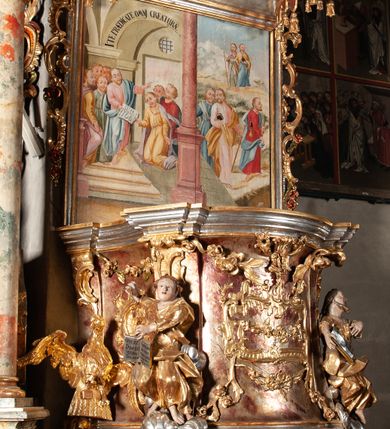 Zdjęcie nr 1: Ambona przyścienna, wisząca, z wejściem od tyłu dwubiegowymi schodami z podestem. Kosz na rzucie owalu o wklęsłych ściankach bocznych i wypukłej frontowej, na wypukłym cokole zdobionym od frontu płaskorzeźbionym motywem rocaille’u. U spodu kosza pięć kabłąków dekorowanych u góry palmetami i fragmentami rocaille’ów, zakończonych zwisem w formie winnego grona. Ścianki kosza opięte wklęsłym pilastrami; od frontu z figurami św. Jana i św. Mateusza siedzących na obłokach, trzymających otwarte księgi z napisem: OVI EX DEO EST VERBA DEI AUDIT / PROPTEREA VOS NON AUDITIS, QVIA EX DEO NON ESTIS. Joanne 8,47; oraz: ERAT ENIM / DOCENS EOS / SICUT PO=/TESTATEM /HABENS / ET NON / SICUT / SCRIBAE / EORUM / ET PHARI=/SAEI. Mat 7,18; na tle pozostałych pilastrów symbole ewangelistów: orzeł trzymający w ‘szponach kałamarz oraz głowa wołu. Ścianki w polach dekorowane rocaille’ami, frontowa z różanymi gałązkami. Kosz zwieńczony profilowanym gzymsem, występującym nad pilastrami. Na zaplecku obraz Szymona Kawalskiego Rozesłanie Apostołów, w kształcie leżącego prostokąta, w profilowanej, złoconej ramie, ujęty uszami utworzonymi z motywów rocaille’ów. Baldachim powtarza rzut kosza, wsparty na belkowaniu dekorowanym palmetami i rocaille’ami w partii fryzu, z podwieszonym lambrekinem. Powyżej ażurowa konstrukcja z wolut dekorowanych rocaille’ami, zbliżona do korony, otaczająca półpostać Chrystusa trzymającego jabłko królewskie i laskę pasterską. U spodu baldachimu podwieszona Gołębica Ducha Świętego w glorii. Struktura marmoryzowana laserunkowo, profile srebrzone, ornamenty złocone.