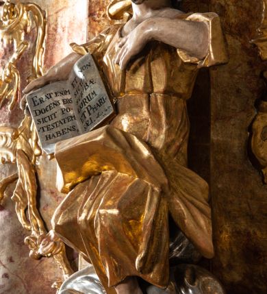 Zdjęcie nr 7: Ambona przyścienna, wisząca, z wejściem od tyłu dwubiegowymi schodami z podestem. Kosz na rzucie owalu o wklęsłych ściankach bocznych i wypukłej frontowej, na wypukłym cokole zdobionym od frontu płaskorzeźbionym motywem rocaille’u. U spodu kosza pięć kabłąków dekorowanych u góry palmetami i fragmentami rocaille’ów, zakończonych zwisem w formie winnego grona. Ścianki kosza opięte wklęsłym pilastrami; od frontu z figurami św. Jana i św. Mateusza siedzących na obłokach, trzymających otwarte księgi z napisem: OVI EX DEO EST VERBA DEI AUDIT / PROPTEREA VOS NON AUDITIS, QVIA EX DEO NON ESTIS. Joanne 8,47; oraz: ERAT ENIM / DOCENS EOS / SICUT PO=/TESTATEM /HABENS / ET NON / SICUT / SCRIBAE / EORUM / ET PHARI=/SAEI. Mat 7,18; na tle pozostałych pilastrów symbole ewangelistów: orzeł trzymający w ‘szponach kałamarz oraz głowa wołu. Ścianki w polach dekorowane rocaille’ami, frontowa z różanymi gałązkami. Kosz zwieńczony profilowanym gzymsem, występującym nad pilastrami. Na zaplecku obraz Szymona Kawalskiego Rozesłanie Apostołów, w kształcie leżącego prostokąta, w profilowanej, złoconej ramie, ujęty uszami utworzonymi z motywów rocaille’ów. Baldachim powtarza rzut kosza, wsparty na belkowaniu dekorowanym palmetami i rocaille’ami w partii fryzu, z podwieszonym lambrekinem. Powyżej ażurowa konstrukcja z wolut dekorowanych rocaille’ami, zbliżona do korony, otaczająca półpostać Chrystusa trzymającego jabłko królewskie i laskę pasterską. U spodu baldachimu podwieszona Gołębica Ducha Świętego w glorii. Struktura marmoryzowana laserunkowo, profile srebrzone, ornamenty złocone.
