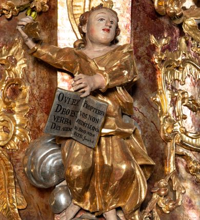 Zdjęcie nr 9: Ambona przyścienna, wisząca, z wejściem od tyłu dwubiegowymi schodami z podestem. Kosz na rzucie owalu o wklęsłych ściankach bocznych i wypukłej frontowej, na wypukłym cokole zdobionym od frontu płaskorzeźbionym motywem rocaille’u. U spodu kosza pięć kabłąków dekorowanych u góry palmetami i fragmentami rocaille’ów, zakończonych zwisem w formie winnego grona. Ścianki kosza opięte wklęsłym pilastrami; od frontu z figurami św. Jana i św. Mateusza siedzących na obłokach, trzymających otwarte księgi z napisem: OVI EX DEO EST VERBA DEI AUDIT / PROPTEREA VOS NON AUDITIS, QVIA EX DEO NON ESTIS. Joanne 8,47; oraz: ERAT ENIM / DOCENS EOS / SICUT PO=/TESTATEM /HABENS / ET NON / SICUT / SCRIBAE / EORUM / ET PHARI=/SAEI. Mat 7,18; na tle pozostałych pilastrów symbole ewangelistów: orzeł trzymający w ‘szponach kałamarz oraz głowa wołu. Ścianki w polach dekorowane rocaille’ami, frontowa z różanymi gałązkami. Kosz zwieńczony profilowanym gzymsem, występującym nad pilastrami. Na zaplecku obraz Szymona Kawalskiego Rozesłanie Apostołów, w kształcie leżącego prostokąta, w profilowanej, złoconej ramie, ujęty uszami utworzonymi z motywów rocaille’ów. Baldachim powtarza rzut kosza, wsparty na belkowaniu dekorowanym palmetami i rocaille’ami w partii fryzu, z podwieszonym lambrekinem. Powyżej ażurowa konstrukcja z wolut dekorowanych rocaille’ami, zbliżona do korony, otaczająca półpostać Chrystusa trzymającego jabłko królewskie i laskę pasterską. U spodu baldachimu podwieszona Gołębica Ducha Świętego w glorii. Struktura marmoryzowana laserunkowo, profile srebrzone, ornamenty złocone.