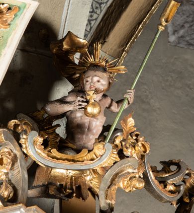 Zdjęcie nr 13: Ambona przyścienna, wisząca, z wejściem od tyłu dwubiegowymi schodami z podestem. Kosz na rzucie owalu o wklęsłych ściankach bocznych i wypukłej frontowej, na wypukłym cokole zdobionym od frontu płaskorzeźbionym motywem rocaille’u. U spodu kosza pięć kabłąków dekorowanych u góry palmetami i fragmentami rocaille’ów, zakończonych zwisem w formie winnego grona. Ścianki kosza opięte wklęsłym pilastrami; od frontu z figurami św. Jana i św. Mateusza siedzących na obłokach, trzymających otwarte księgi z napisem: OVI EX DEO EST VERBA DEI AUDIT / PROPTEREA VOS NON AUDITIS, QVIA EX DEO NON ESTIS. Joanne 8,47; oraz: ERAT ENIM / DOCENS EOS / SICUT PO=/TESTATEM /HABENS / ET NON / SICUT / SCRIBAE / EORUM / ET PHARI=/SAEI. Mat 7,18; na tle pozostałych pilastrów symbole ewangelistów: orzeł trzymający w ‘szponach kałamarz oraz głowa wołu. Ścianki w polach dekorowane rocaille’ami, frontowa z różanymi gałązkami. Kosz zwieńczony profilowanym gzymsem, występującym nad pilastrami. Na zaplecku obraz Szymona Kawalskiego Rozesłanie Apostołów, w kształcie leżącego prostokąta, w profilowanej, złoconej ramie, ujęty uszami utworzonymi z motywów rocaille’ów. Baldachim powtarza rzut kosza, wsparty na belkowaniu dekorowanym palmetami i rocaille’ami w partii fryzu, z podwieszonym lambrekinem. Powyżej ażurowa konstrukcja z wolut dekorowanych rocaille’ami, zbliżona do korony, otaczająca półpostać Chrystusa trzymającego jabłko królewskie i laskę pasterską. U spodu baldachimu podwieszona Gołębica Ducha Świętego w glorii. Struktura marmoryzowana laserunkowo, profile srebrzone, ornamenty złocone.