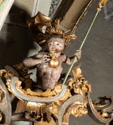 Zdjęcie nr 14: Ambona przyścienna, wisząca, z wejściem od tyłu dwubiegowymi schodami z podestem. Kosz na rzucie owalu o wklęsłych ściankach bocznych i wypukłej frontowej, na wypukłym cokole zdobionym od frontu płaskorzeźbionym motywem rocaille’u. U spodu kosza pięć kabłąków dekorowanych u góry palmetami i fragmentami rocaille’ów, zakończonych zwisem w formie winnego grona. Ścianki kosza opięte wklęsłym pilastrami; od frontu z figurami św. Jana i św. Mateusza siedzących na obłokach, trzymających otwarte księgi z napisem: OVI EX DEO EST VERBA DEI AUDIT / PROPTEREA VOS NON AUDITIS, QVIA EX DEO NON ESTIS. Joanne 8,47; oraz: ERAT ENIM / DOCENS EOS / SICUT PO=/TESTATEM /HABENS / ET NON / SICUT / SCRIBAE / EORUM / ET PHARI=/SAEI. Mat 7,18; na tle pozostałych pilastrów symbole ewangelistów: orzeł trzymający w ‘szponach kałamarz oraz głowa wołu. Ścianki w polach dekorowane rocaille’ami, frontowa z różanymi gałązkami. Kosz zwieńczony profilowanym gzymsem, występującym nad pilastrami. Na zaplecku obraz Szymona Kawalskiego Rozesłanie Apostołów, w kształcie leżącego prostokąta, w profilowanej, złoconej ramie, ujęty uszami utworzonymi z motywów rocaille’ów. Baldachim powtarza rzut kosza, wsparty na belkowaniu dekorowanym palmetami i rocaille’ami w partii fryzu, z podwieszonym lambrekinem. Powyżej ażurowa konstrukcja z wolut dekorowanych rocaille’ami, zbliżona do korony, otaczająca półpostać Chrystusa trzymającego jabłko królewskie i laskę pasterską. U spodu baldachimu podwieszona Gołębica Ducha Świętego w glorii. Struktura marmoryzowana laserunkowo, profile srebrzone, ornamenty złocone.