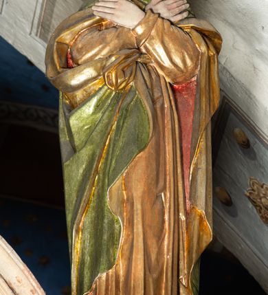 Zdjęcie nr 5: Belka profilowana, o formie pełnego belkowania, wygięta faliście, pośrodku wyłamana łukiem półkolistym nadwieszonym. Od frontu fryz dekorowany akantem i rozetami; od strony prezbiterium data: 1770; od spodu dekorowana rozetami. Na belce Grupa Ukrzyżowania. Rzeźby pełnoplastyczne, polichromowane. Pośrodku krzyż z figurą martwego Chrystusa. Ciało w lekkim zwisie, o szeroko rozłożonych ramionach. Kolana delikatnie ugięte, stopy przebite jednym gwoździem, założone prawa na lewą. Ciało wychudzone, smukłe, o podkreślonej muskulaturze, z zaznaczonymi śladami męki. Twarz pociągła, szczupła, oczy zamknięte; okolona zarostem. Włosy długie, opadające na ramiona. Na głowie korona cierniowa. Perizonium krótkie, ściśle opinające biodra, delikatnie drapowanie, ze zwisem tkaniny przy prawym boku. Na górnej belce krzyża titulus w formie kartusza z literami: INRI. U dołu krzyża klęcząca św. Maria Magdalena zwróconej en trois quarts w lewo, z głową skierowaną ku górze. Lewą ręką przytrzymuje stopę Chrystusa, prawa wyciągnięta przed siebie. Włosy upięte z tyłu głowy. Ubrana w bogatą suknię z gorsetem i dekoracyjnych rękawach oraz płaszcz zarzucony na ramiona. Po prawej stronie krzyża Matki Boska, ukazana frontalnie, z delikatnie pochylona głową i dłońmi złożonymi w geście modlitwy. Twarz pociągła, z uwypuklonym podbródkiem. Maria ubrana w suknię oraz płaszcz przewiązany na lewym ramieniu. Na głowie welon. Po lewej stronie krzyża św. Jan Ewangelista, ukazany en face, z głową skierowaną ku górze i dłońmi skrzyżowanymi na piersi. Twarz pociągła o młodzieńczych rysach, włosy długie, kręcone. Ubrany w długa tunikę przewiązaną w talii oraz płaszcz przewiązany na lewym ramieniu. Polichromia naturalistyczna w odsłoniętych partiach ciała, szaty złocone z laserunkiem.