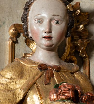 Zdjęcie nr 4: Rzeźba pełnoplastyczna, przyścienna, z tyłu drążona, ustawiona na niskim postumencie na rzucie kwadratu. Figura ukazana bokiem w stosunku do widza, zwrócona w lewo ku środkowi ołtarza, stojąca w kontrapoście, o esowato wygiętej sylwetce. W lewej, wyciągniętej w bok ręce trzyma palmę męczeństwa, prawą przytula do piersi kosz z różami. Twarz okrągła, szeroka, niewielkie oczy i nos, usta delikatnie rozchylone, wydatny podbródek. Włosy upięte z tyłu, na głowie korona otwarta. Ubrana w długą, delikatnie drapowaną, ściśle przylegająca do ciała suknię z krótkimi rękawami, gorset oraz płaszcz, delikatnie drapowany, przewiązany na piersi, opadający na plecy i upięty na lewym biodrze. Polichromia naturalistyczna w odsłoniętych partiach ciała, szaty i atrybuty złocone.