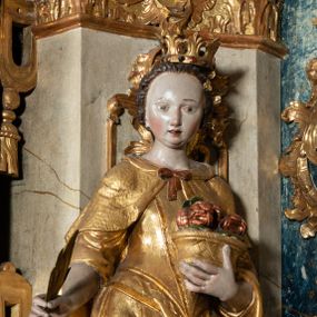 Zdjęcie nr 1: Rzeźba pełnoplastyczna, przyścienna, z tyłu drążona, ustawiona na niskim postumencie na rzucie kwadratu. Figura ukazana bokiem w stosunku do widza, zwrócona w lewo ku środkowi ołtarza, stojąca w kontrapoście, o esowato wygiętej sylwetce. W lewej, wyciągniętej w bok ręce trzyma palmę męczeństwa, prawą przytula do piersi kosz z różami. Twarz okrągła, szeroka, niewielkie oczy i nos, usta delikatnie rozchylone, wydatny podbródek. Włosy upięte z tyłu, na głowie korona otwarta. Ubrana w długą, delikatnie drapowaną, ściśle przylegająca do ciała suknię z krótkimi rękawami, gorset oraz płaszcz, delikatnie drapowany, przewiązany na piersi, opadający na plecy i upięty na lewym biodrze. Polichromia naturalistyczna w odsłoniętych partiach ciała, szaty i atrybuty złocone.
