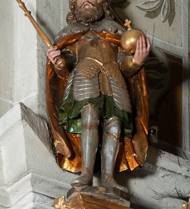 Zdjęcie nr 2: Rzeźba pełnoplastyczna, z tyłu drążona, ustawiona na niskiej podstawie. Święty stoi w kontrapoście, bokiem, z tułowiem skręconym w prawo, w kierunku widza; w lewej ręce trzyma jabłko królewskie, w prawej berło. Twarz pociągła o delikatnych rysach, okolona długa brodą. Włosy długie, kręcone, opadają na ramiona, na głowie korona zamknięta z krzyżem. Ubrany w pełną, łuskową zbroję oraz płaszcz spięty na piersi i opadający na plecy. Polichromia naturalistyczna w odsłoniętych partiach ciała, zbroja srebrzona, płaszcz laserunkowy, atrybuty złocone.