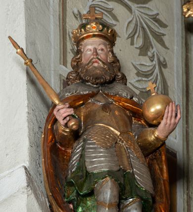 Zdjęcie nr 1: Rzeźba pełnoplastyczna, z tyłu drążona, ustawiona na niskiej podstawie. Święty stoi w kontrapoście, bokiem, z tułowiem skręconym w prawo, w kierunku widza; w lewej ręce trzyma jabłko królewskie, w prawej berło. Twarz pociągła o delikatnych rysach, okolona długa brodą. Włosy długie, kręcone, opadają na ramiona, na głowie korona zamknięta z krzyżem. Ubrany w pełną, łuskową zbroję oraz płaszcz spięty na piersi i opadający na plecy. Polichromia naturalistyczna w odsłoniętych partiach ciała, zbroja srebrzona, płaszcz laserunkowy, atrybuty złocone.