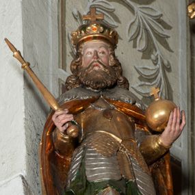 Zdjęcie nr 1: Rzeźba pełnoplastyczna, z tyłu drążona, ustawiona na niskiej podstawie. Święty stoi w kontrapoście, bokiem, z tułowiem skręconym w prawo, w kierunku widza; w lewej ręce trzyma jabłko królewskie, w prawej berło. Twarz pociągła o delikatnych rysach, okolona długa brodą. Włosy długie, kręcone, opadają na ramiona, na głowie korona zamknięta z krzyżem. Ubrany w pełną, łuskową zbroję oraz płaszcz spięty na piersi i opadający na plecy. Polichromia naturalistyczna w odsłoniętych partiach ciała, zbroja srebrzona, płaszcz laserunkowy, atrybuty złocone.
