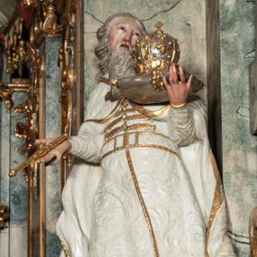 Zdjęcie nr 1: Rzeźba pełnoplastyczna, przyścienna, z tyłu drążona, na niskim postumencie.  Figura zwrócona en face, o delikatnie skręconej, przechylonej w tył sylwetce; głowa skierowana w lewą stronę, delikatnie uniesiona. Lewą ręką ugiętą, wyciągniętą przed siebie, podtrzymuje poduszkę z koroną zamkniętą; prawą ugiętą, wyciągniętą w bok, trzyma berło. Twarz okrągła, oczy zmrużone, patrzące do góry, nos długi, prosty, usta delikatnie rozchylone; okolona długą brodą o skręconych puklach, opadająca na pierś. Włosy długie, z przedziałkiem na środku głowy, skręcone w grube pukle. Święty ubrany w spodnie i wysokie buty; kaftan z wzorzystej, płaskorzeźbionej tkaniny, zapinany na guzy, z pasem i złoconą lamówką; płaszcz spięty na piersi, opadający przez ramiona na boki, o zawijających się brzegach. Polichromia naturalistyczna w odsłoniętych partiach ciała, szaty białe, atrybuty i detale stroju złocone.