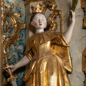 Zdjęcie nr 1: Rzeźba pełnoplastyczna, przyścienna, z tyłu drążona, ustawiona na niskim postumencie na rzucie kwadratu. Święta, ukazana w en trois quatrs, zwrócona w prawo, z głową skierowaną w lewo, stoi w kontrapoście, delikatnie przechylona do tyłu. W lewej, uniesionej ręce trzyma palmę męczeństwa, w prawej miecz, skierowany ostrzem w dół. Przy jej prawym boku koło. Twarz okrągła, szeroka, niewielkie oczy i nos, usta delikatnie rozchylone. Włosy upięte z tyłu, na głowie korona otwarta. Ubrana w długą suknię spodnią z krótkimi rękawami, suknie wierzchnią z gorsetem, sięgającą kolan dekorowaną rytymi pasami z koronkowym brzegiem, oraz płaszcz, delikatnie drapowany, przewiązany na piersi, opadający na plecy i upięty na prawym biodrze. Polichromia naturalistyczna w odsłoniętych partiach ciała, szaty i atrybuty złocone.