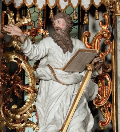 Zdjęcie nr 1: Rzeźba pełnoplastyczna, przyścienna, z tyłu drążona. Święty ukazany frontalnie, z głową zwróconą w prawo, w kierunku środka ołtarza. Prawa ręka uniesiona, wyciągnięta w bok, lewą, ugiętą, podtrzymuje opartą na biodrze zamkniętą księgę i miecz zwrócony ostrzem w dół. Twarz pociągła, o starczych rysach, oczy niewielkie, długi prosty nos, usta rozchylone; okolona długą brodą o skręconych puklach, opadającą na pierś. Włosy krótkie, gęste, kręcone. Święty obrany w tunikę obficie marszczoną w partii torsu oraz płaszcz, gęsto drapowany w grube fałdy, przewieszony przez lewe ramię i opadający na kolana. Polichromia naturalistyczna w odsłoniętych partiach ciała, szaty białe, atrybuty i detale stroju złocone.