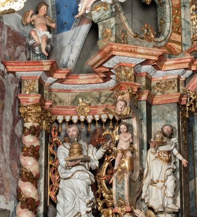 Zdjęcie nr 4: Rzeźba pełnoplastyczna, przyścienna, z tyłu, drążona, ustawiona na rzeźbionym fragmencie skały. Święty ukazany frontalnie, z prawą nogą ugiętą, opartą o skałę. Prawą rękę podtrzymuje przed sobą zamkniętą księgę z potrójną papieską tiarą; w lewej, wyciągniętej w bok ręce trzyma dwa skrzyżowane klucze. Twarz pociągła, o starczych rysach, niewielkich oczach, prostym długim nosie, niewielkich, rozchylonych ustach, okolona krótką, kręconą brodą. Włosy krótkie, kręcone, pukle po bokach i na czubku głowy. Święty ubrany w tunikę z kołnierzem, przepasaną w talii, marszczoną w gęste drobne fałdki, oraz płaszcz przerzucony przez lewe ramię i opadający gęstymi, grubymi fałdami, skręconej i ekspresyjnie rozwianej tkaniny na kolana i prawy bok. Polichromia naturalistyczna w odsłoniętych partiach ciała, szaty białe, atrybuty i detale stroju złocone.