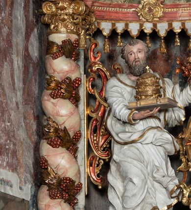 Zdjęcie nr 3: Rzeźba pełnoplastyczna, przyścienna, z tyłu, drążona, ustawiona na rzeźbionym fragmencie skały. Święty ukazany frontalnie, z prawą nogą ugiętą, opartą o skałę. Prawą rękę podtrzymuje przed sobą zamkniętą księgę z potrójną papieską tiarą; w lewej, wyciągniętej w bok ręce trzyma dwa skrzyżowane klucze. Twarz pociągła, o starczych rysach, niewielkich oczach, prostym długim nosie, niewielkich, rozchylonych ustach, okolona krótką, kręconą brodą. Włosy krótkie, kręcone, pukle po bokach i na czubku głowy. Święty ubrany w tunikę z kołnierzem, przepasaną w talii, marszczoną w gęste drobne fałdki, oraz płaszcz przerzucony przez lewe ramię i opadający gęstymi, grubymi fałdami, skręconej i ekspresyjnie rozwianej tkaniny na kolana i prawy bok. Polichromia naturalistyczna w odsłoniętych partiach ciała, szaty białe, atrybuty i detale stroju złocone.