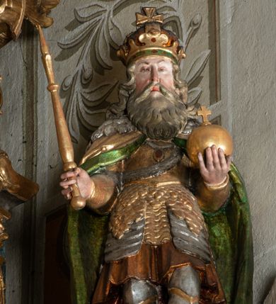 Zdjęcie nr 1: Rzeźba pełnoplastyczna, przyścienna, z tyłu drążona, ustawiona na niskiej podstawie. Święty ukazany en trois quarts, stoi w kontrapoście, w lewej ręce trzyma jabłko królewskie, w prawej berło. Twarz pociągła, o delikatnych rysach, okolona długą brodą. Włosy długie, kręcone, opadają na ramiona, na głowie korona zamknięta z krzyżem. Ubrany w pełną zbroję oraz płaszcz spięty na piersi i opadający na plecy. Polichromia naturalistyczna w odsłoniętych partiach ciała, zbroja srebrzona, płaszcz laserunkowy, atrybuty złocone.
