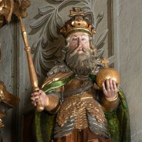 Zdjęcie nr 1: Rzeźba pełnoplastyczna, przyścienna, z tyłu drążona, ustawiona na niskiej podstawie. Święty ukazany en trois quarts, stoi w kontrapoście, w lewej ręce trzyma jabłko królewskie, w prawej berło. Twarz pociągła, o delikatnych rysach, okolona długą brodą. Włosy długie, kręcone, opadają na ramiona, na głowie korona zamknięta z krzyżem. Ubrany w pełną zbroję oraz płaszcz spięty na piersi i opadający na plecy. Polichromia naturalistyczna w odsłoniętych partiach ciała, zbroja srebrzona, płaszcz laserunkowy, atrybuty złocone.