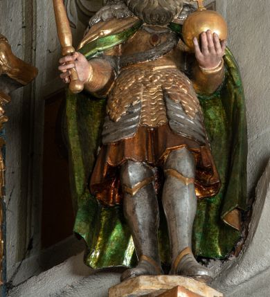 Zdjęcie nr 2: Rzeźba pełnoplastyczna, przyścienna, z tyłu drążona, ustawiona na niskiej podstawie. Święty ukazany en trois quarts, stoi w kontrapoście, w lewej ręce trzyma jabłko królewskie, w prawej berło. Twarz pociągła, o delikatnych rysach, okolona długą brodą. Włosy długie, kręcone, opadają na ramiona, na głowie korona zamknięta z krzyżem. Ubrany w pełną zbroję oraz płaszcz spięty na piersi i opadający na plecy. Polichromia naturalistyczna w odsłoniętych partiach ciała, zbroja srebrzona, płaszcz laserunkowy, atrybuty złocone.