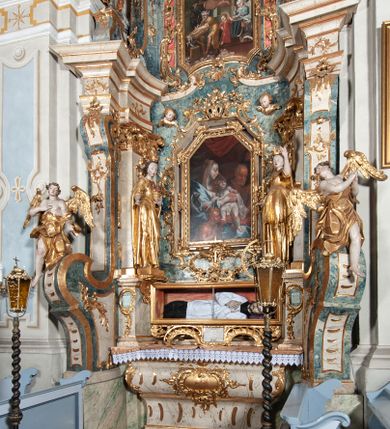 Zdjęcie nr 3: Ołtarz architektoniczny, jednoosiowy, jednokondygnacyjny ze zwieńczeniem, na cokole. Mensa drewniana umieszczona na drewnianej tumbie o wklęsło-wypukłych bokach. Antependium dekorowane rocaille’owym kartuszem z rytym gorejącym sercem, brzegi zdobione rocaille’em. W predelli przeszklona trumienka z figurą św. Jana Nepomucena, w profilowanej, złoconej ramie, na rocaillowej podstawie. Nastawa ujęta parami występujących do przodu filarów: wewnętrzne filary opięte pilastrami; zewnętrzne filary z wolutami zamiast trzonów, z figurami aniołów. Podpory dźwigają pełne belkowanie, przerwane nad polem środkowym. W polu nisza w kształcie stojącego prostokąta zamkniętego trójbocznie, w której obraz Święta Rodzina w profilowanej ramie. Przy filarach od wewnątrz rocaille’owe konsole z figurami św. Doroty i św. Katarzyny Aleksandryjskiej. Zwieńczenie w formie aedikuli zbliżonej do kwadratu o fantazyjnym wklęsło-wypukłym zamknięciu; ujęte pilastrami przechodzącymi w spływy wolutowe, opadające na belkowanie, tworzące postumenty dla figur św. Stefana i św. Emeryka. W polu zwieńczenia obraz z przedstawieniem Świętej Rodziny przy pracy, w kształcie kwadratu o wklęsłych narożach, w profilowanej ramie. Zwieńczenie zamknięte glorią promienistą z literami IHS w otoczeniu obłoków; na osi pilastrów rokokowe wazony z różami.W partii cokołów kanony w rocaille’owych ramach. Trzony pilastrów i woluty dekorowane rocaille’owymi płycinami, we fryzie rocaille. Nisza w polu środkowym ujęta rocaille’ami, zwieńczona mitrą książęcą, flankowana przez parę uskrzydlonych główek anielskich. Woluty zwieńczenia dekorowane motywami rocaille’ów. Rama obrazu w polu ujęta małżowiną, ornamentem roślinnym i rocaille’ami. Struktura marmoryzowana w odcieniu jasnoniebieskim, podpory, tumba i cokoły w odcieniu kości słoniowej; ornamentyka i profile złocone.
