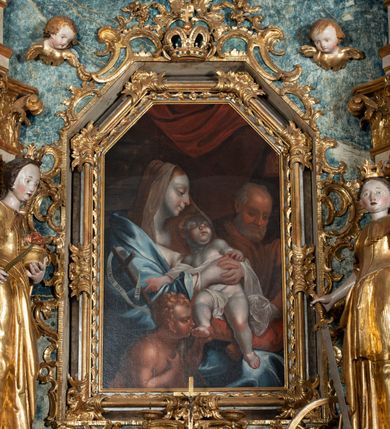 Zdjęcie nr 5: Ołtarz architektoniczny, jednoosiowy, jednokondygnacyjny ze zwieńczeniem, na cokole. Mensa drewniana umieszczona na drewnianej tumbie o wklęsło-wypukłych bokach. Antependium dekorowane rocaille’owym kartuszem z rytym gorejącym sercem, brzegi zdobione rocaille’em. W predelli przeszklona trumienka z figurą św. Jana Nepomucena, w profilowanej, złoconej ramie, na rocaillowej podstawie. Nastawa ujęta parami występujących do przodu filarów: wewnętrzne filary opięte pilastrami; zewnętrzne filary z wolutami zamiast trzonów, z figurami aniołów. Podpory dźwigają pełne belkowanie, przerwane nad polem środkowym. W polu nisza w kształcie stojącego prostokąta zamkniętego trójbocznie, w której obraz Święta Rodzina w profilowanej ramie. Przy filarach od wewnątrz rocaille’owe konsole z figurami św. Doroty i św. Katarzyny Aleksandryjskiej. Zwieńczenie w formie aedikuli zbliżonej do kwadratu o fantazyjnym wklęsło-wypukłym zamknięciu; ujęte pilastrami przechodzącymi w spływy wolutowe, opadające na belkowanie, tworzące postumenty dla figur św. Stefana i św. Emeryka. W polu zwieńczenia obraz z przedstawieniem Świętej Rodziny przy pracy, w kształcie kwadratu o wklęsłych narożach, w profilowanej ramie. Zwieńczenie zamknięte glorią promienistą z literami IHS w otoczeniu obłoków; na osi pilastrów rokokowe wazony z różami.W partii cokołów kanony w rocaille’owych ramach. Trzony pilastrów i woluty dekorowane rocaille’owymi płycinami, we fryzie rocaille. Nisza w polu środkowym ujęta rocaille’ami, zwieńczona mitrą książęcą, flankowana przez parę uskrzydlonych główek anielskich. Woluty zwieńczenia dekorowane motywami rocaille’ów. Rama obrazu w polu ujęta małżowiną, ornamentem roślinnym i rocaille’ami. Struktura marmoryzowana w odcieniu jasnoniebieskim, podpory, tumba i cokoły w odcieniu kości słoniowej; ornamentyka i profile złocone.