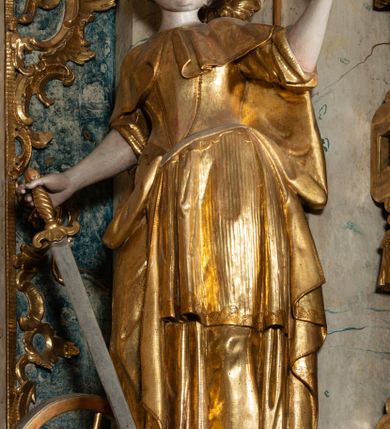 Zdjęcie nr 20: Ołtarz architektoniczny, jednoosiowy, jednokondygnacyjny ze zwieńczeniem, na cokole. Mensa drewniana umieszczona na drewnianej tumbie o wklęsło-wypukłych bokach. Antependium dekorowane rocaille’owym kartuszem z rytym gorejącym sercem, brzegi zdobione rocaille’em. W predelli przeszklona trumienka z figurą św. Jana Nepomucena, w profilowanej, złoconej ramie, na rocaillowej podstawie. Nastawa ujęta parami występujących do przodu filarów: wewnętrzne filary opięte pilastrami; zewnętrzne filary z wolutami zamiast trzonów, z figurami aniołów. Podpory dźwigają pełne belkowanie, przerwane nad polem środkowym. W polu nisza w kształcie stojącego prostokąta zamkniętego trójbocznie, w której obraz Święta Rodzina w profilowanej ramie. Przy filarach od wewnątrz rocaille’owe konsole z figurami św. Doroty i św. Katarzyny Aleksandryjskiej. Zwieńczenie w formie aedikuli zbliżonej do kwadratu o fantazyjnym wklęsło-wypukłym zamknięciu; ujęte pilastrami przechodzącymi w spływy wolutowe, opadające na belkowanie, tworzące postumenty dla figur św. Stefana i św. Emeryka. W polu zwieńczenia obraz z przedstawieniem Świętej Rodziny przy pracy, w kształcie kwadratu o wklęsłych narożach, w profilowanej ramie. Zwieńczenie zamknięte glorią promienistą z literami IHS w otoczeniu obłoków; na osi pilastrów rokokowe wazony z różami.W partii cokołów kanony w rocaille’owych ramach. Trzony pilastrów i woluty dekorowane rocaille’owymi płycinami, we fryzie rocaille. Nisza w polu środkowym ujęta rocaille’ami, zwieńczona mitrą książęcą, flankowana przez parę uskrzydlonych główek anielskich. Woluty zwieńczenia dekorowane motywami rocaille’ów. Rama obrazu w polu ujęta małżowiną, ornamentem roślinnym i rocaille’ami. Struktura marmoryzowana w odcieniu jasnoniebieskim, podpory, tumba i cokoły w odcieniu kości słoniowej; ornamentyka i profile złocone.