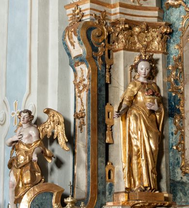 Zdjęcie nr 25: Ołtarz architektoniczny, jednoosiowy, jednokondygnacyjny ze zwieńczeniem, na cokole. Mensa drewniana umieszczona na drewnianej tumbie o wklęsło-wypukłych bokach. Antependium dekorowane rocaille’owym kartuszem z rytym gorejącym sercem, brzegi zdobione rocaille’em. W predelli przeszklona trumienka z figurą św. Jana Nepomucena, w profilowanej, złoconej ramie, na rocaillowej podstawie. Nastawa ujęta parami występujących do przodu filarów: wewnętrzne filary opięte pilastrami; zewnętrzne filary z wolutami zamiast trzonów, z figurami aniołów. Podpory dźwigają pełne belkowanie, przerwane nad polem środkowym. W polu nisza w kształcie stojącego prostokąta zamkniętego trójbocznie, w której obraz Święta Rodzina w profilowanej ramie. Przy filarach od wewnątrz rocaille’owe konsole z figurami św. Doroty i św. Katarzyny Aleksandryjskiej. Zwieńczenie w formie aedikuli zbliżonej do kwadratu o fantazyjnym wklęsło-wypukłym zamknięciu; ujęte pilastrami przechodzącymi w spływy wolutowe, opadające na belkowanie, tworzące postumenty dla figur św. Stefana i św. Emeryka. W polu zwieńczenia obraz z przedstawieniem Świętej Rodziny przy pracy, w kształcie kwadratu o wklęsłych narożach, w profilowanej ramie. Zwieńczenie zamknięte glorią promienistą z literami IHS w otoczeniu obłoków; na osi pilastrów rokokowe wazony z różami.W partii cokołów kanony w rocaille’owych ramach. Trzony pilastrów i woluty dekorowane rocaille’owymi płycinami, we fryzie rocaille. Nisza w polu środkowym ujęta rocaille’ami, zwieńczona mitrą książęcą, flankowana przez parę uskrzydlonych główek anielskich. Woluty zwieńczenia dekorowane motywami rocaille’ów. Rama obrazu w polu ujęta małżowiną, ornamentem roślinnym i rocaille’ami. Struktura marmoryzowana w odcieniu jasnoniebieskim, podpory, tumba i cokoły w odcieniu kości słoniowej; ornamentyka i profile złocone.